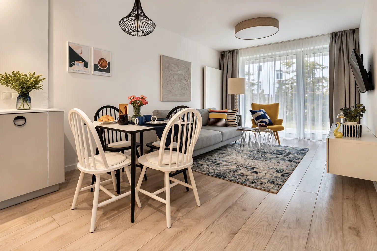 Salon z jadalnią w Apartamencie Mar, czarna lampa wisząca, granatowo-biały dywan, żółty fotel przy oknie, Kołobrzeg