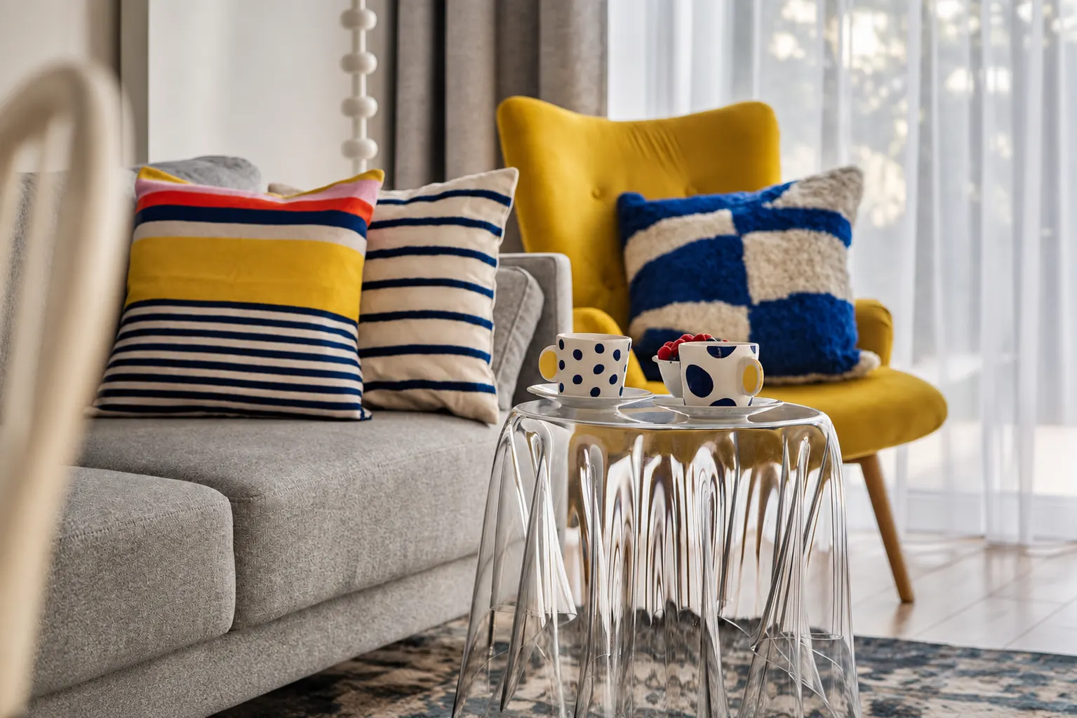 Filiżanki na szklanym stoliku, kolorowe poduszki i żółty fotel, Apartament Mar, Kołobrzeg