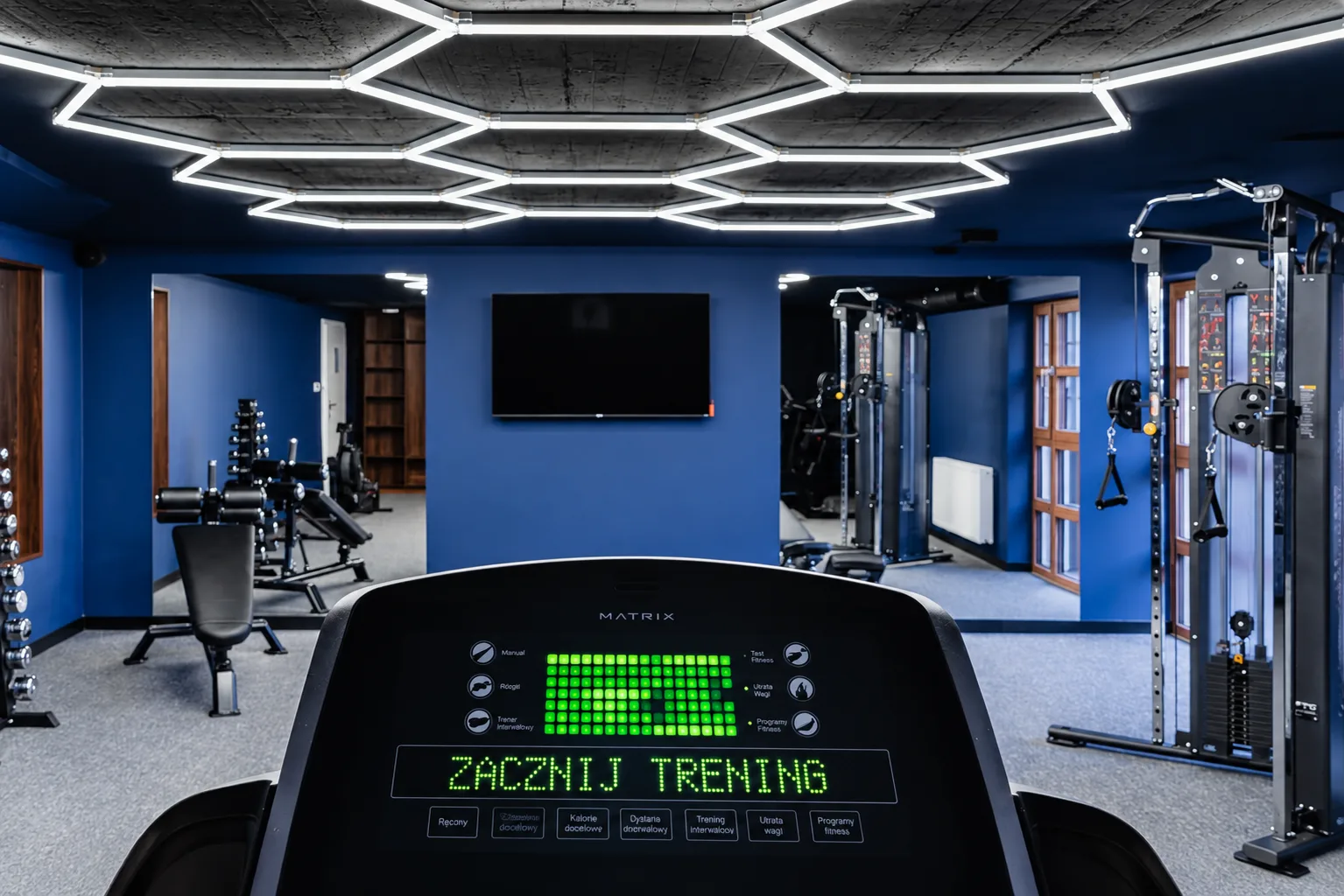 Bieżnia z ekranem i granatowe ściany fitness w apartamentowcu WhiteBlue