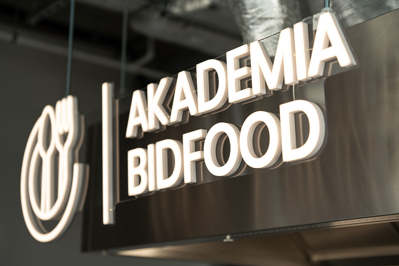 Detal podświetlanego logotypu na ciemnej ścianie, Akademia Bidfood