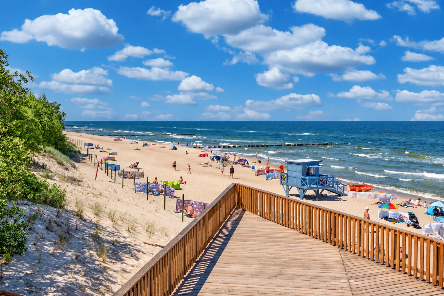 Pomost przez wydmę i szeroka plaża w Rewalu z niebieską wieżą ratowników