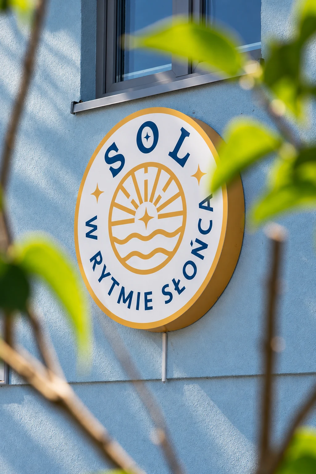 Żółto-niebieskie logo SOL w rytmie słońca na elewacji domku w Trzęsaczu